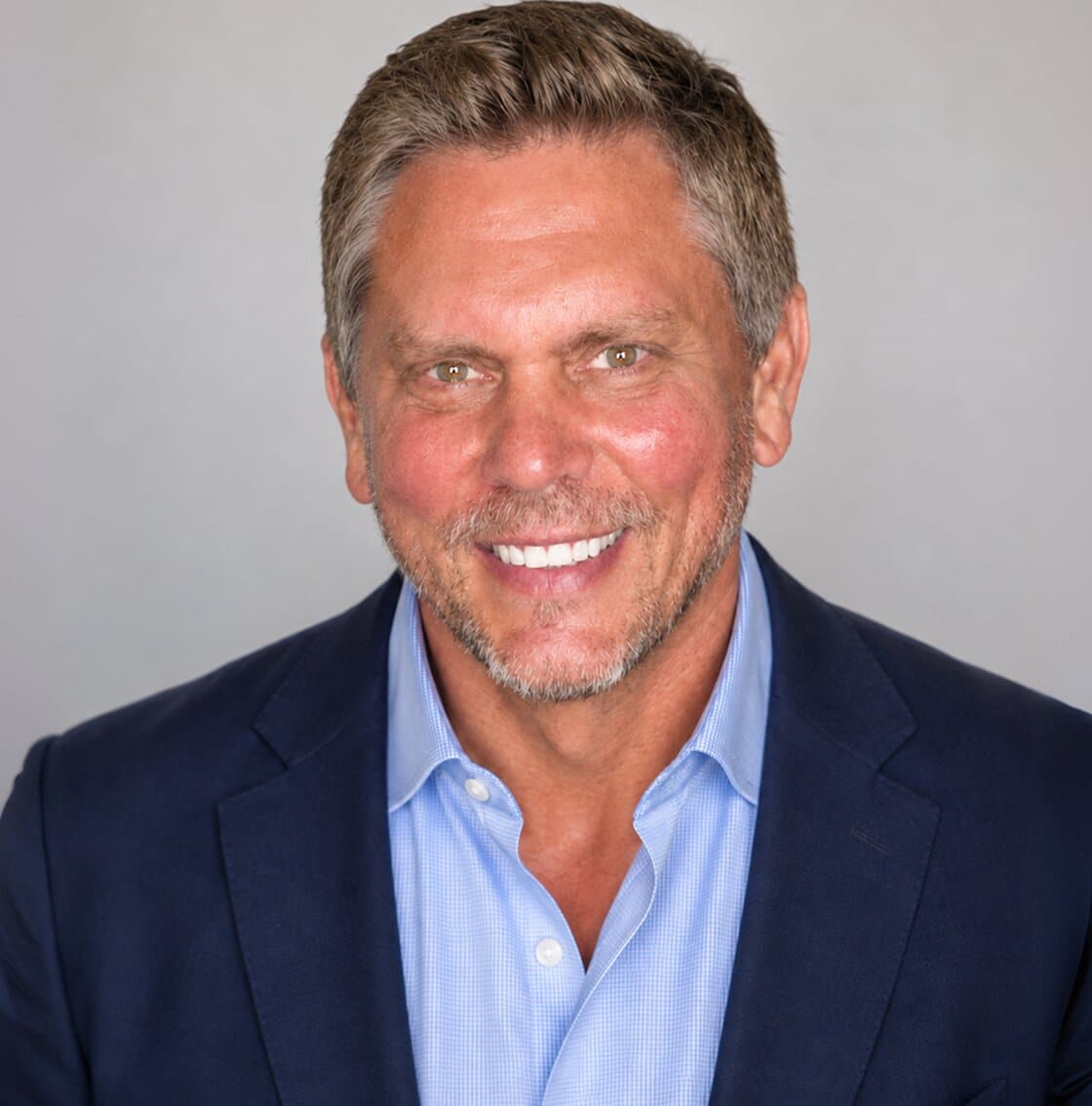 A smiling man with short brown hair, a grey beard, and a blue suit jacket over a light blue shirt.
