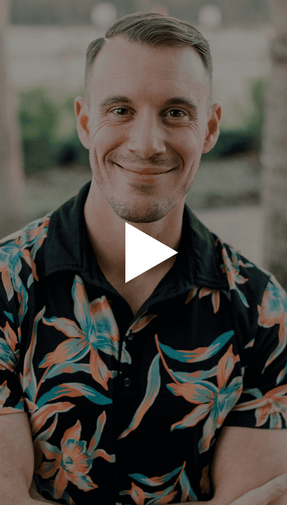 A smiling man with short hair and a floral shirt has a white play button overlayed on his chest.