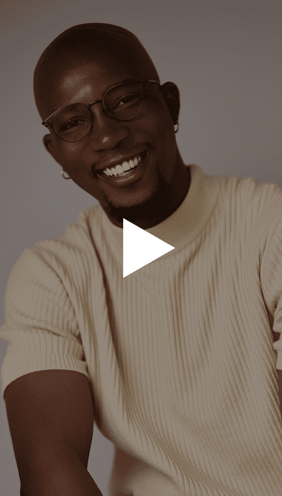 A smiling man with dark skin, glasses, and a light ribbed turtleneck shirt looks at the camera.