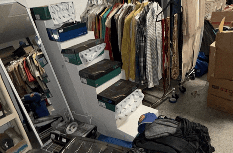 A cluttered room with clothes on racks, shoe boxes on a staircase, and cardboard boxes on the floor.