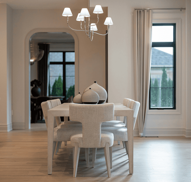 A modern dining room with a light wood table, upholstered chairs, a chandelier, and decorative vases.